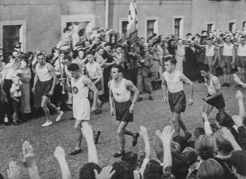Fackelträger und Sportler mit dem olympischen Feuer beim Laufen durch die Straßen von Coswig